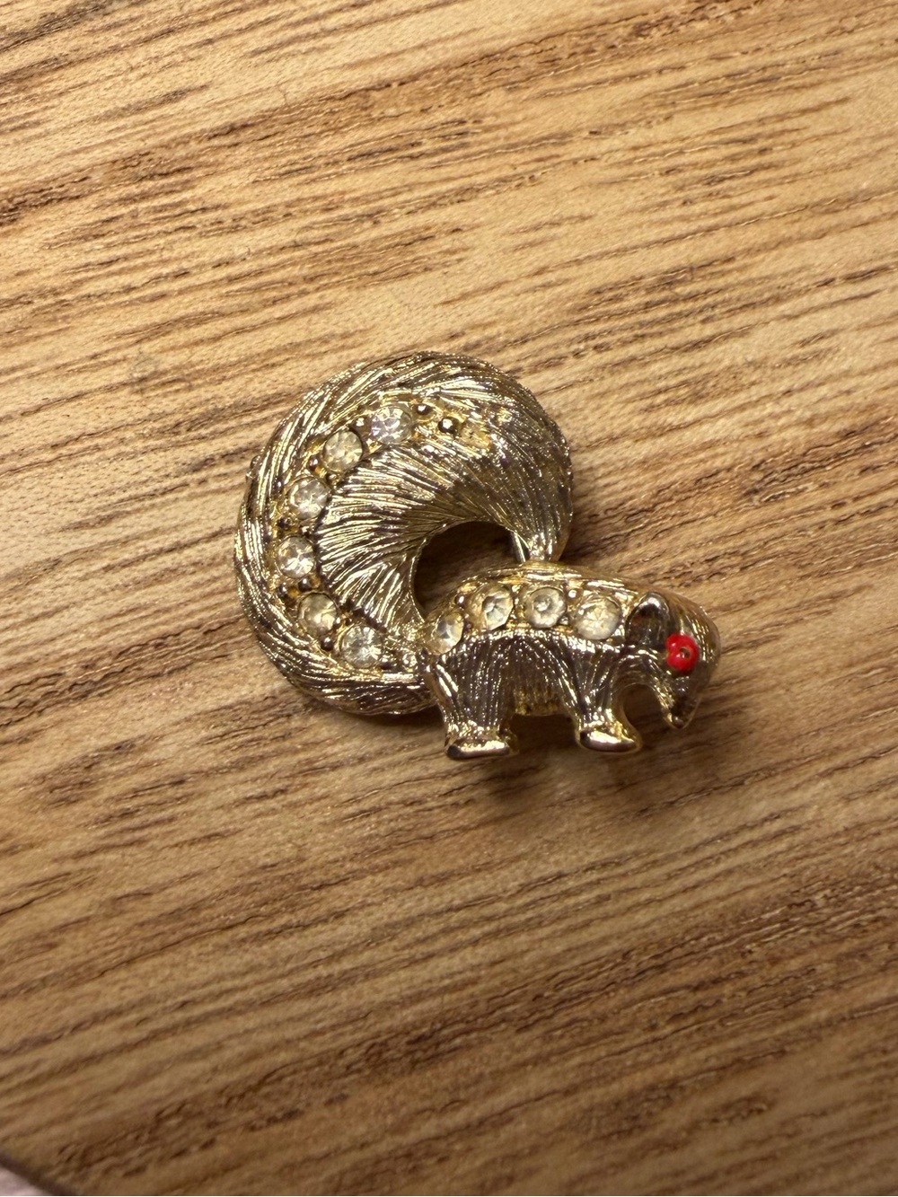 Gold-tone skunk pin brooch with red eyes and faux diamond